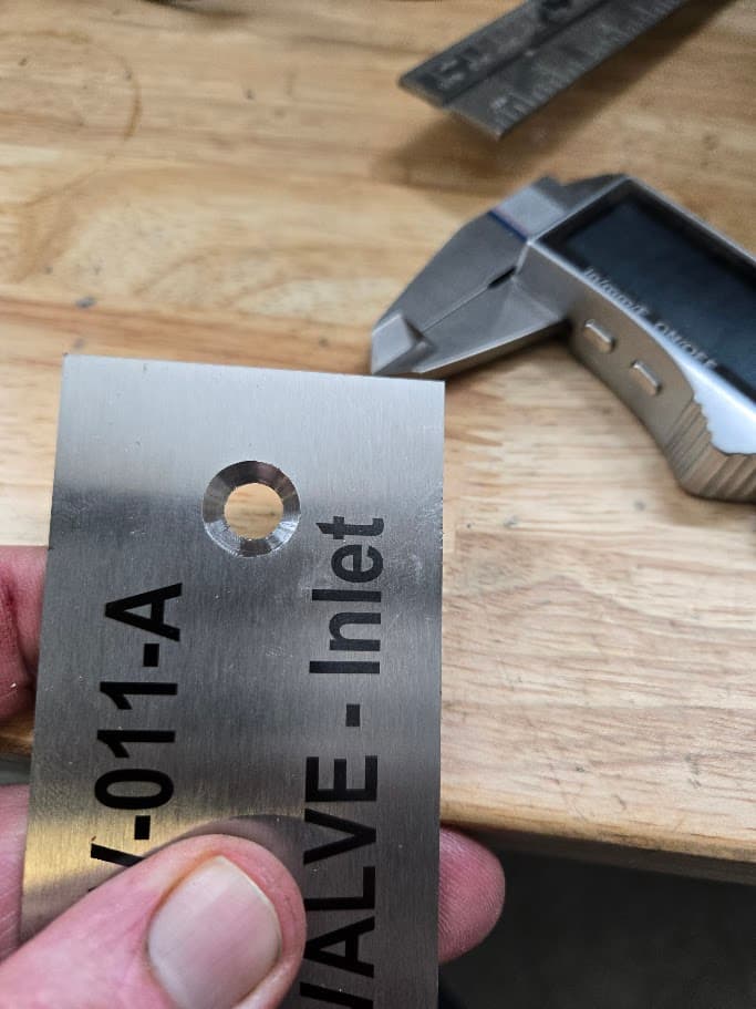 Small bracket batch 001 marked metal tag detail held near digital calipers