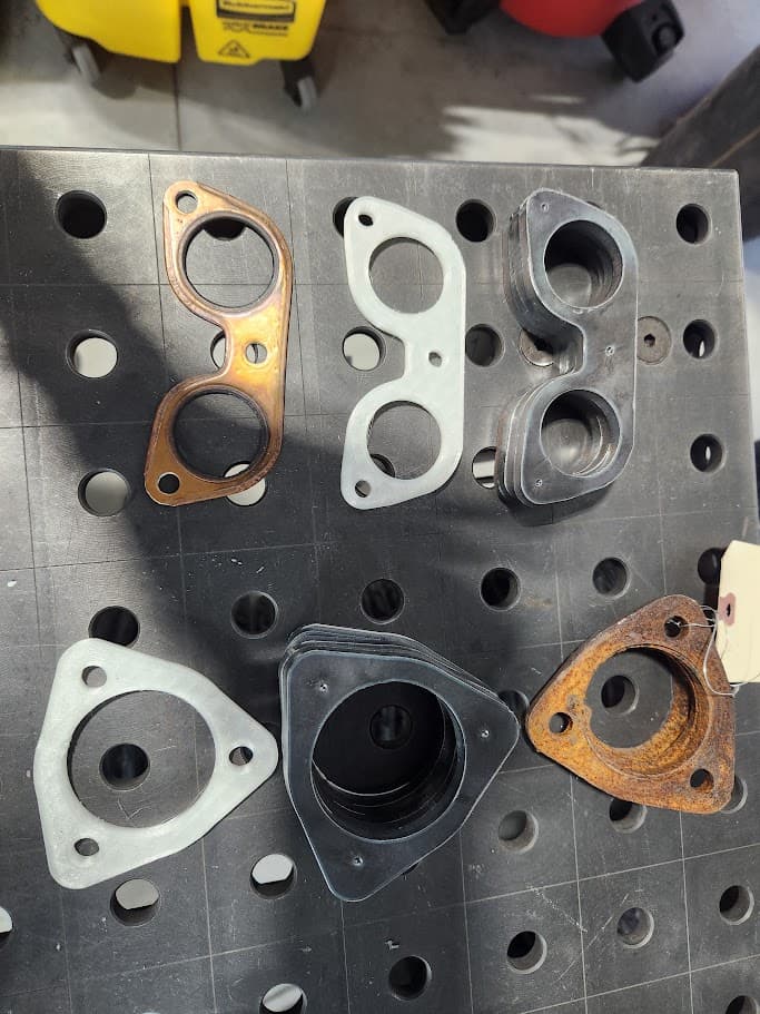 Exhaust spacer plates and small automotive parts laid out on a workbench