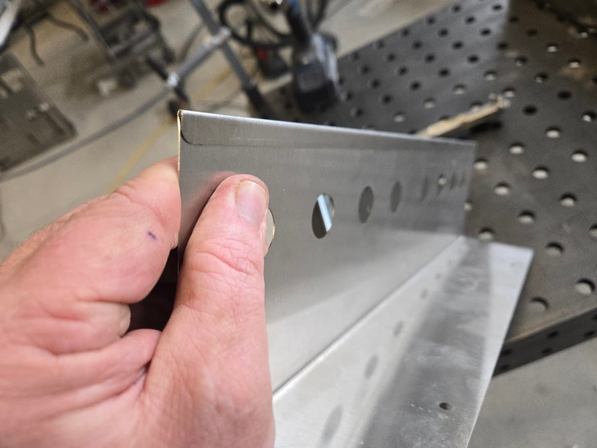 Stainless steel bracket detail held above a fabrication table
